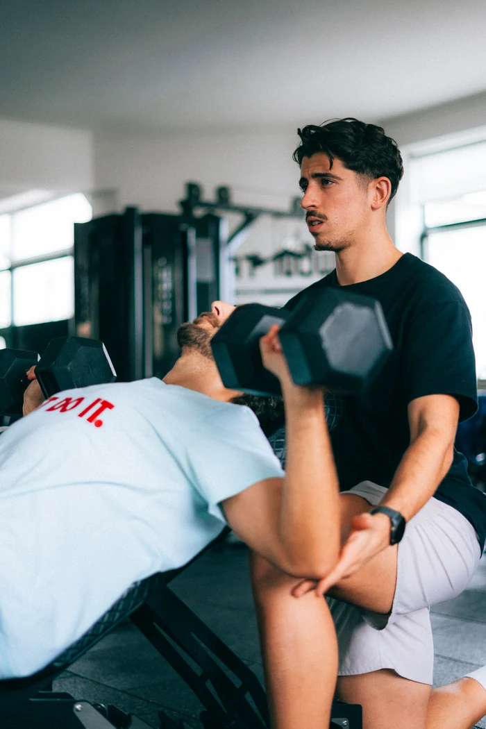Treinador do ShapeUp a acompanhar um aluno com halteres